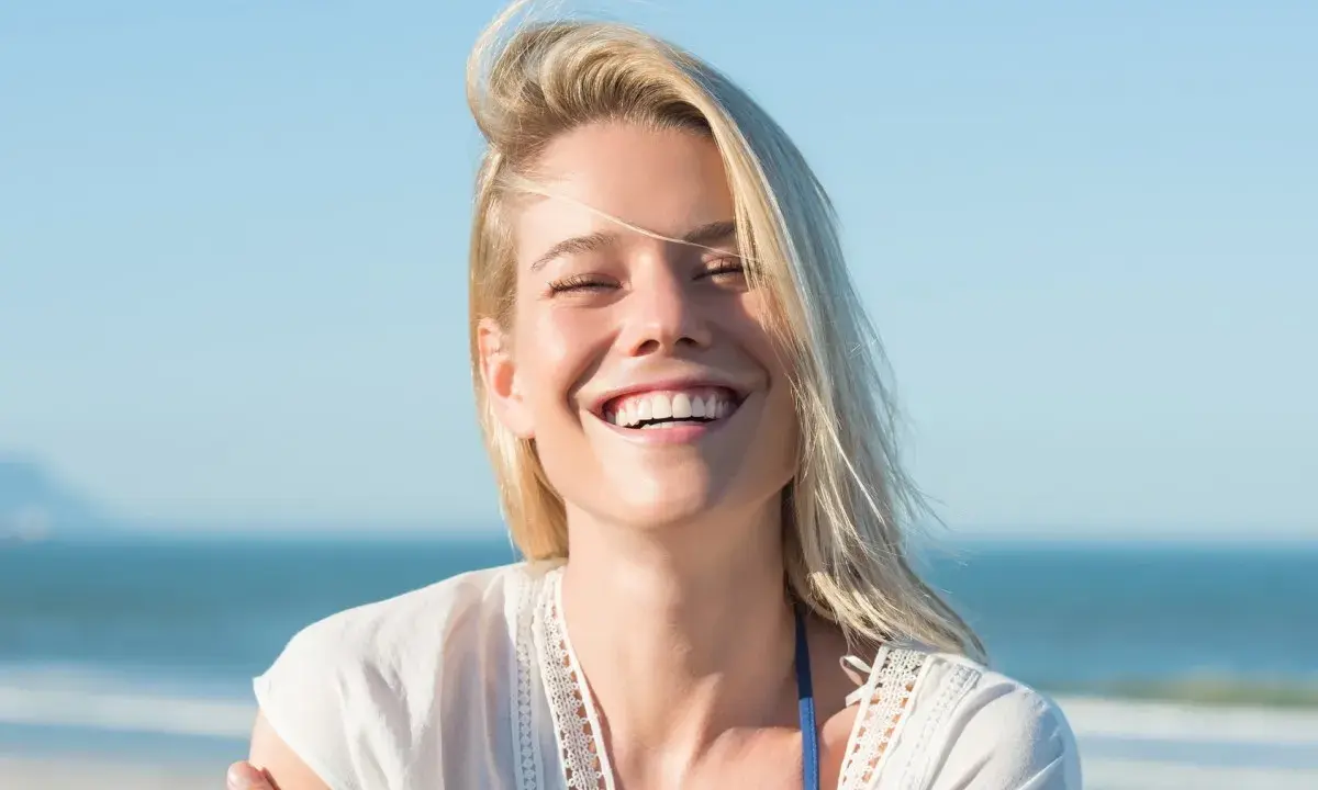 Uśmiechnięta blondynka na plaży, uosobienie tego, kim jest hedonista – ciesząca się chwilą.