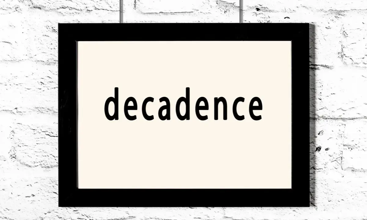 Czarny prostokątny obraz z napisem "decadence" na jasnym tle, wiszący na białej ceglanej ścianie. Symbol dekadentyzmu.