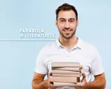 Uśmiechnięty mężczyzna w białej koszulce trzyma stos książek na jasnoniebieskim tle.