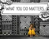 Kobieta siedzi przed muralem z napisem "WHAT YOU DO MATTERS". To inspirujący dialog motywujący.