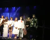 Aktorzy w strojach z epoki, być może z przedstawienia "Dziady cz. 1", stoją na scenie. Jedna z aktorek trzyma mikrofon.