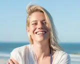 Uśmiechnięta blondynka na plaży, uosobienie tego, kim jest hedonista – ciesząca się chwilą.