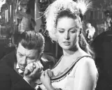 Mężczyzna całuje dłoń kobiety w ozdobnej sukni i pióropuszu. Scena jak z filmu, gdzie piękna lalka budzi namiętność. Non omnis moriar.