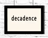 Czarny prostokątny obraz z napisem "decadence" na jasnym tle, wiszący na białej ceglanej ścianie. Symbol dekadentyzmu.