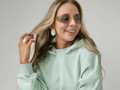Uśmiechnięta blondynka w miętowej bluzie i okularach przeciwsłonecznych, prezentująca swój modny styl.