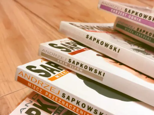 Stos książek Andrzeja Sapkowskiego, idealny przewodnik, jak czytać Wiedźmina. Widoczne tytuły: "Chrzest Ognia", "Wieża Jaskółki", "Czas Pogardy", "Krew Elfów", "Miecz Przeznaczenia".