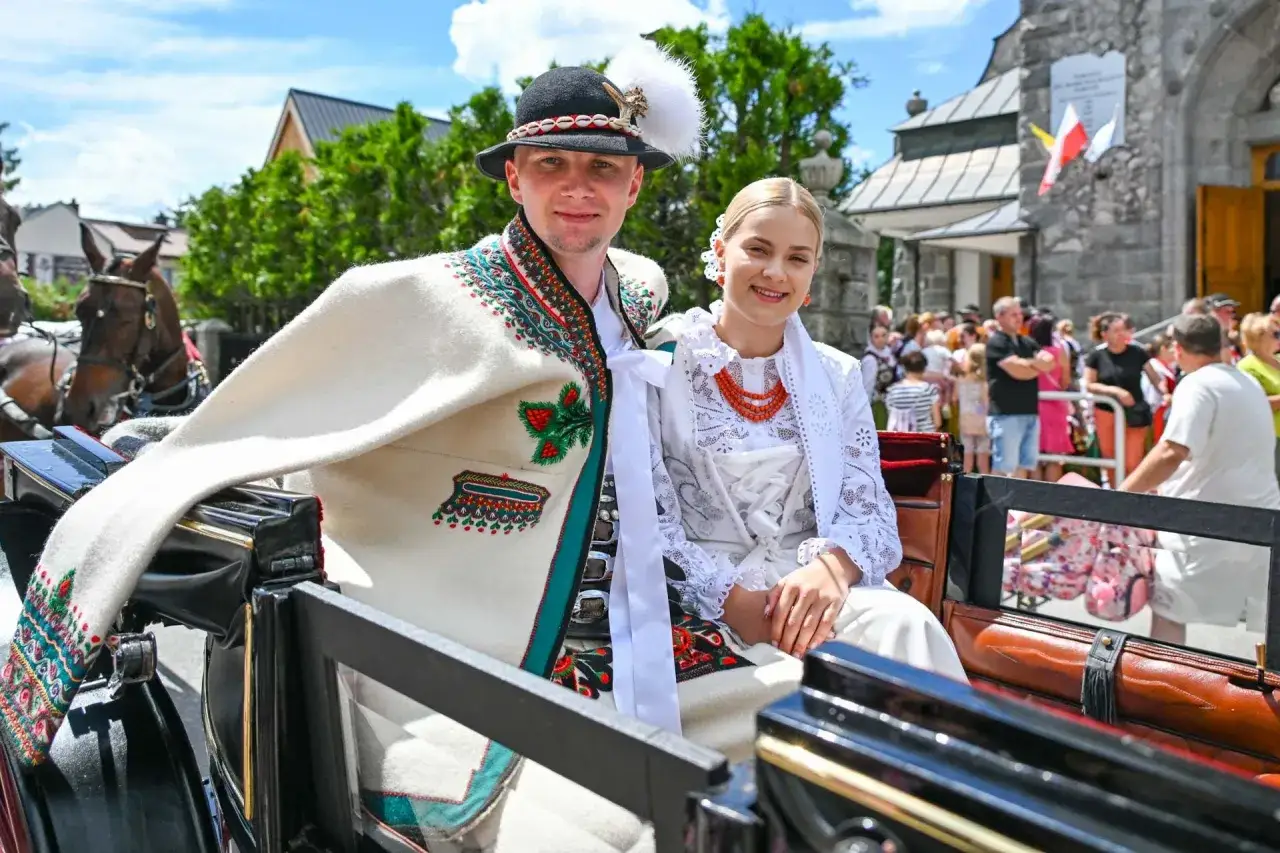Para młoda w tradycyjnych strojach góralskich, z czepcem weselnym na głowie panny młodej, siedzi w bryczce.