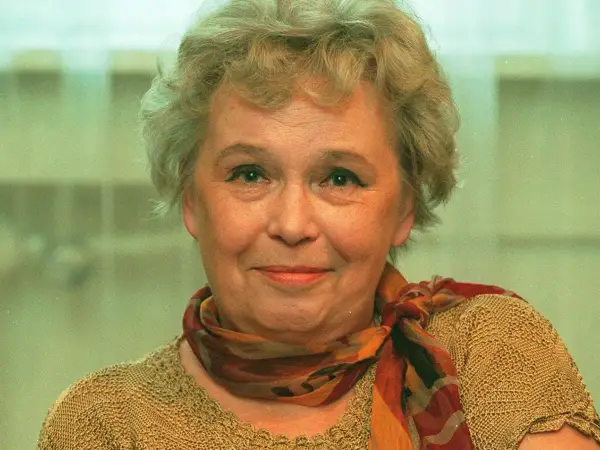 Uśmiechnięta Joanna Chmielewska, autorka kultowych powieści kryminalnych, w beżowym swetrze i kolorowym szalu.
