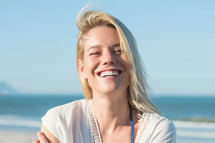 Uśmiechnięta blondynka na plaży, uosobienie tego, kim jest hedonista – ciesząca się chwilą.